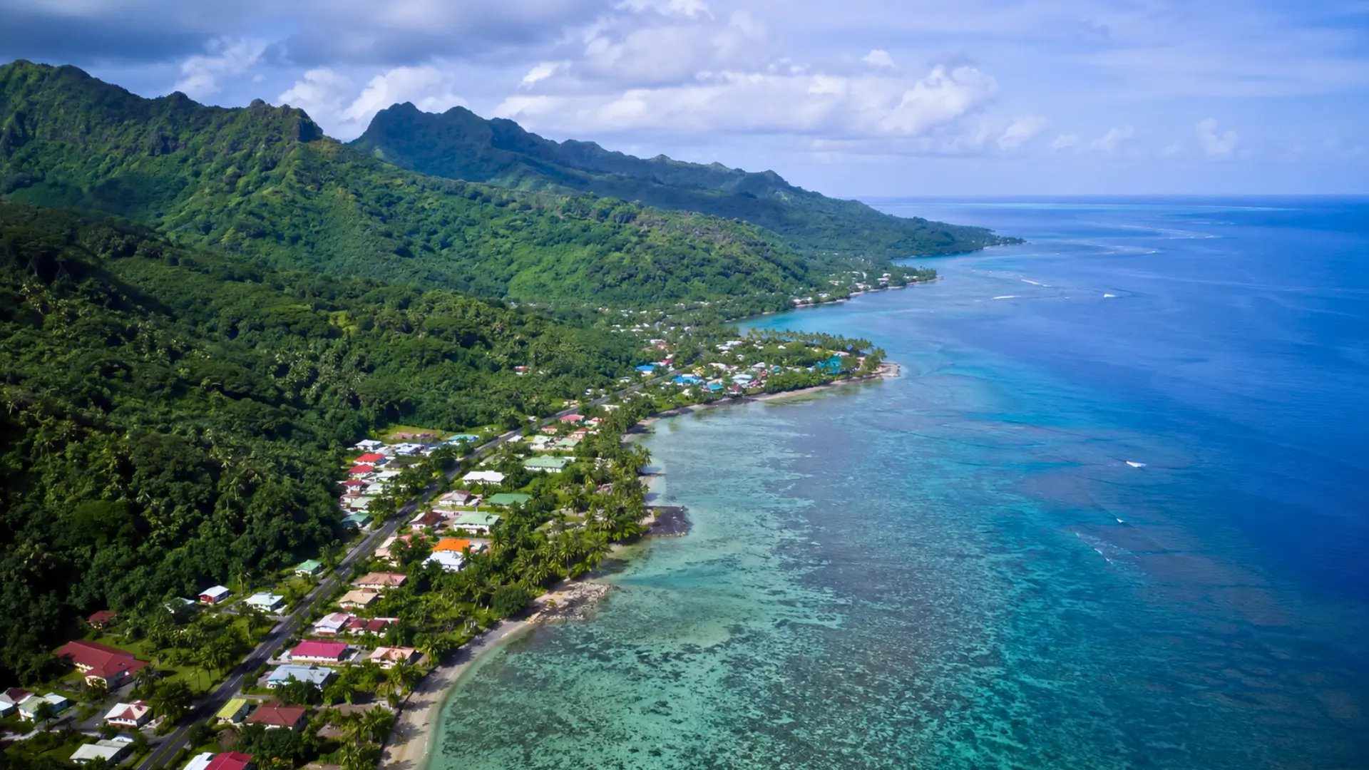 Vue aérienne réaliste d’une île tropicale française avec lagon, récif corallien, forêt dense et habitations le long du littoral.