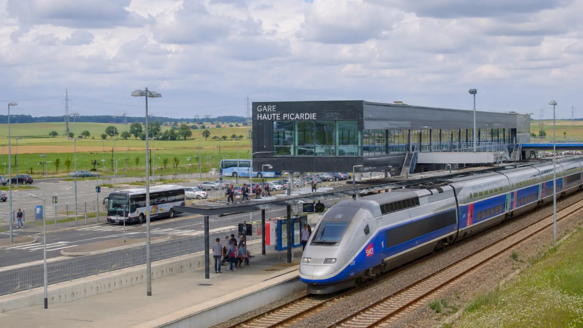 Un TGV à quai devant la gare Haute-Picardie, entourée de parkings, de navettes et de vastes champs picards.