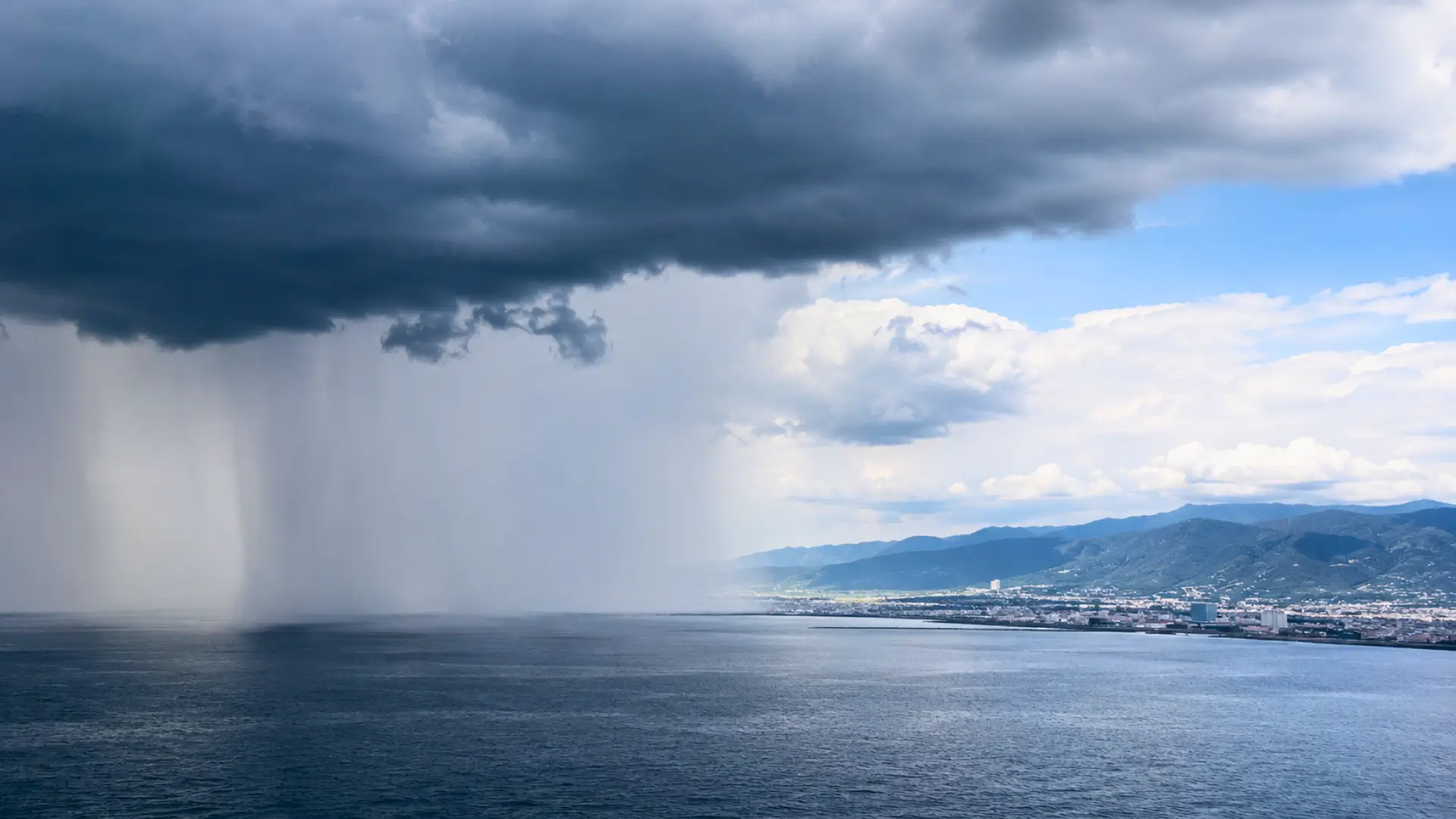 Fortes pluies tombant sur la mer au large d’une ville japonaise sous un imposant nuage d’orage