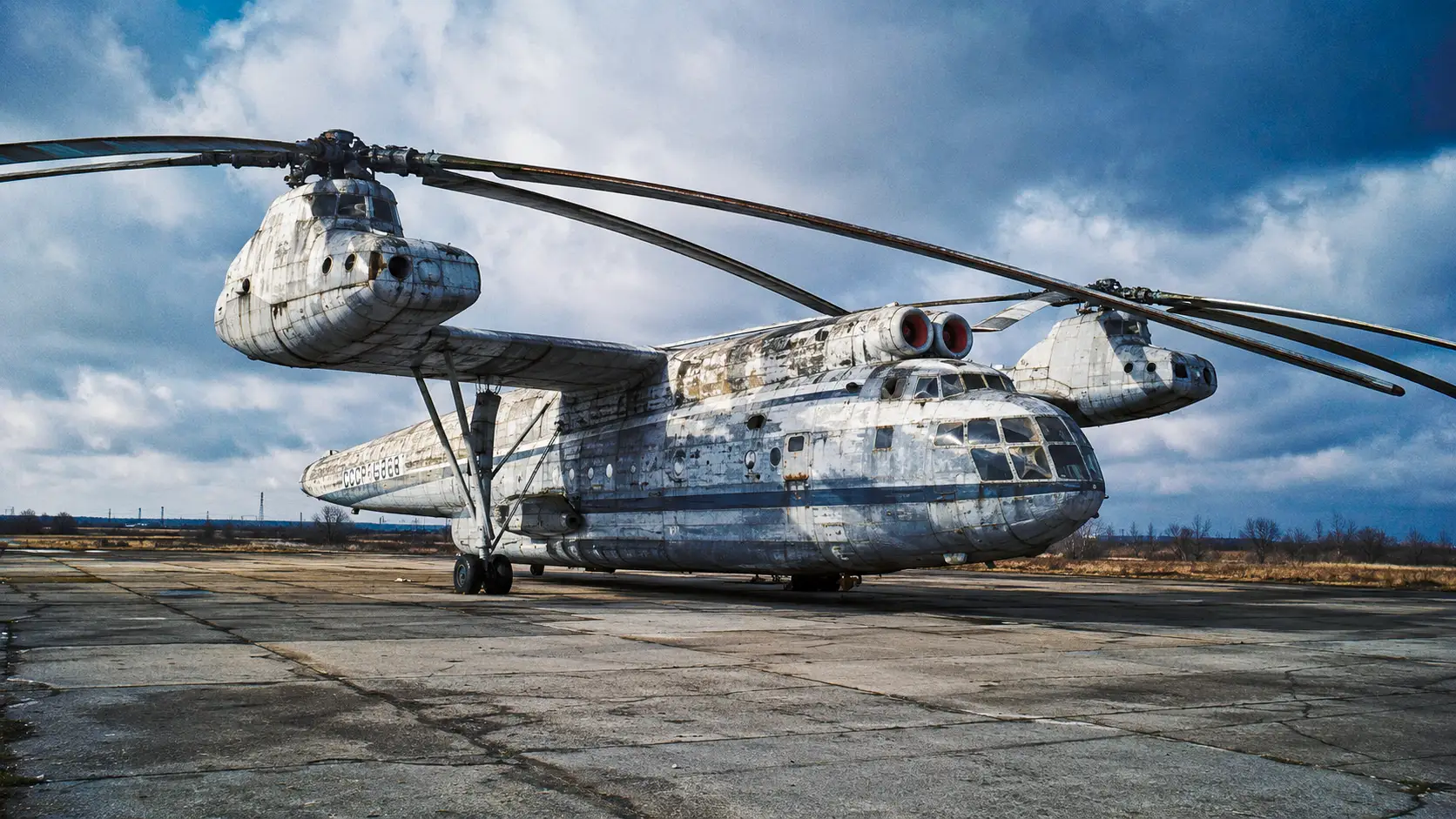 Le gigantesque hélicoptère soviétique Mil V-12 abandonné sur un tarmac russe, marqué par des décennies d’exposition aux intempéries.