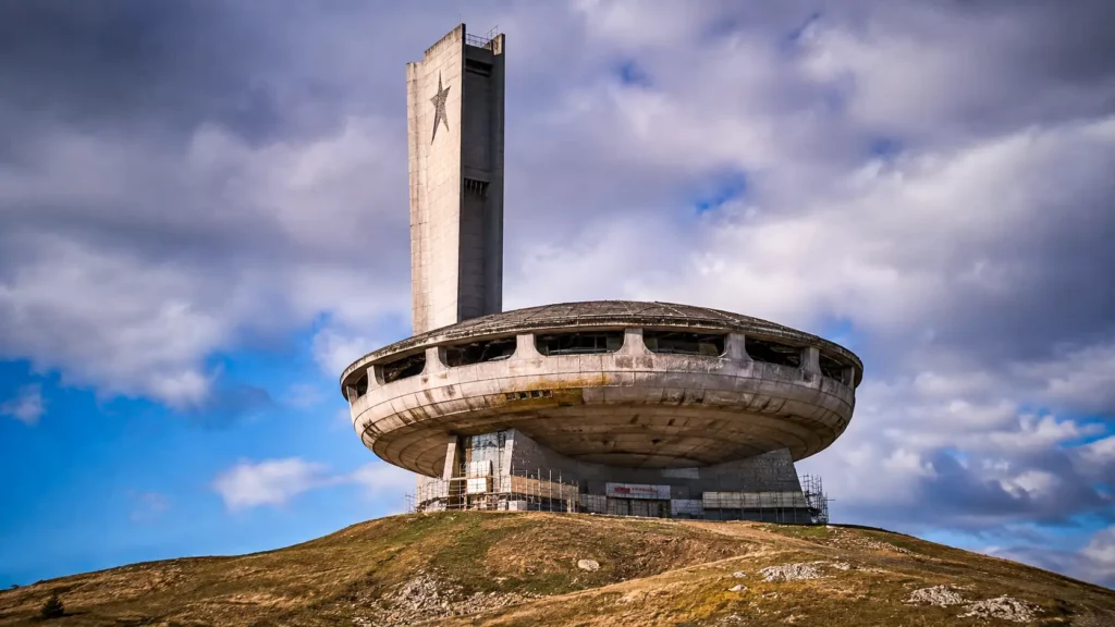Le monument de Buzludzha, imposante structure en forme de soucoupe, domine un sommet montagneux de Bulgarie sous un ciel chargé.