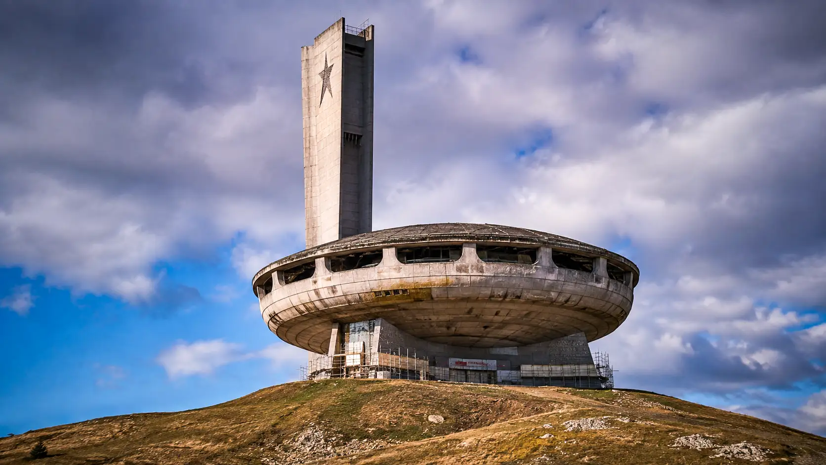 Le monument de Buzludzha, imposante structure en forme de soucoupe, domine un sommet montagneux de Bulgarie sous un ciel chargé.