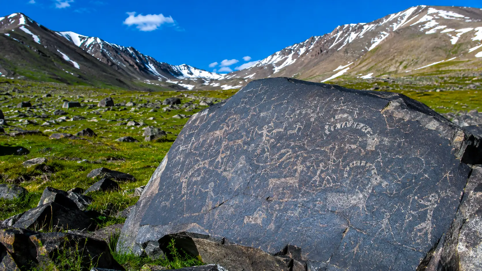 Un grand rocher de basalte couvert de pétroglyphes anciens se dresse dans une vallée montagneuse enneigée du Tian Shan, au Kirghizistan.