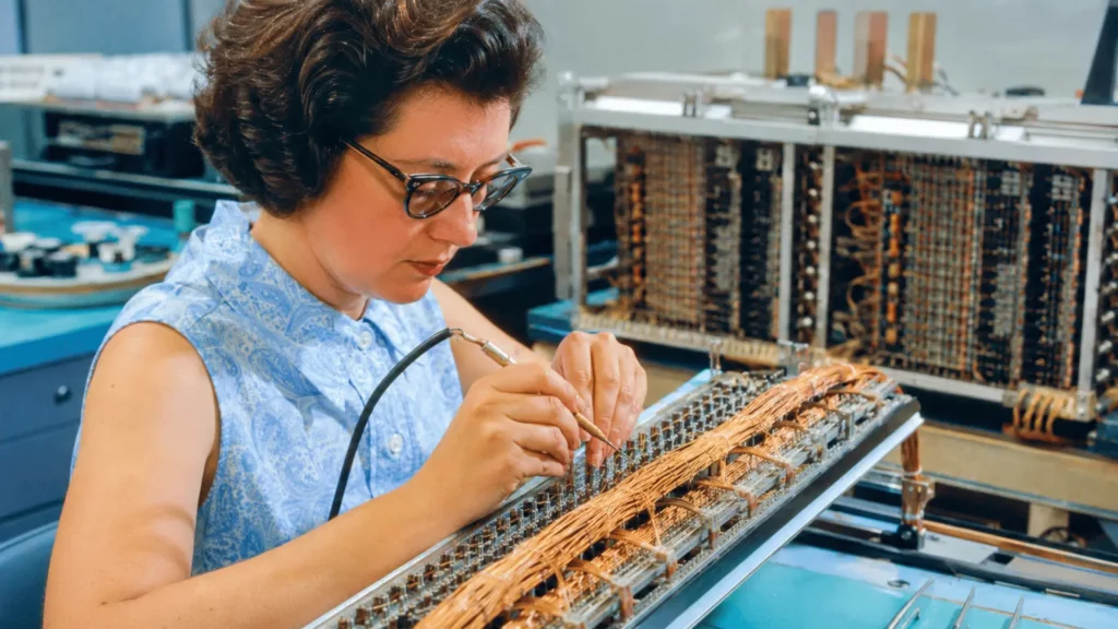 Technicienne assemblant à la main une mémoire à corde de l’ordinateur de guidage Apollo avec des fils de cuivre.