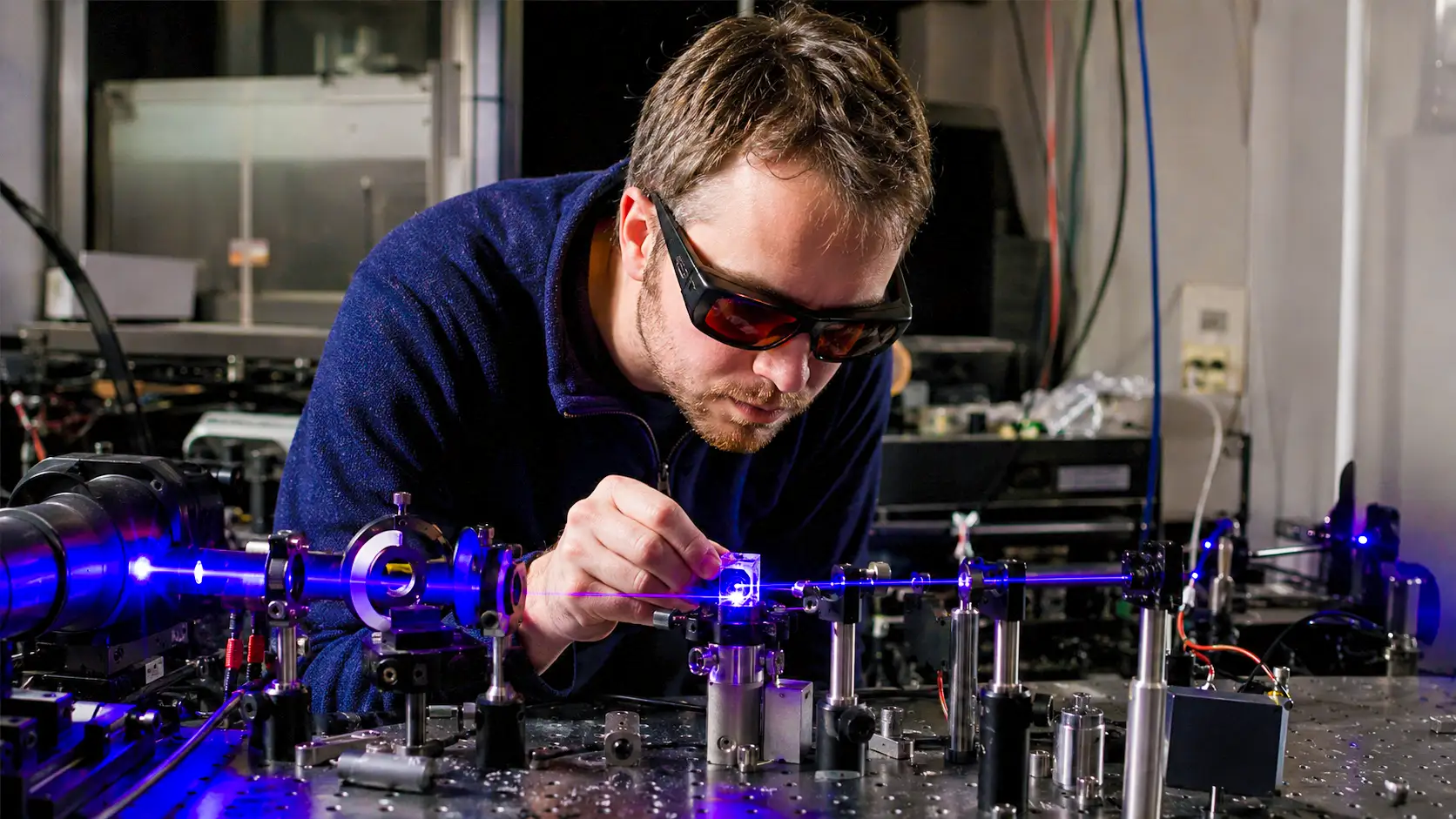 Un physicien ajuste un faisceau laser violet dirigé vers un cristal contenant des atomes de thorium-229 dans un laboratoire d’optique.