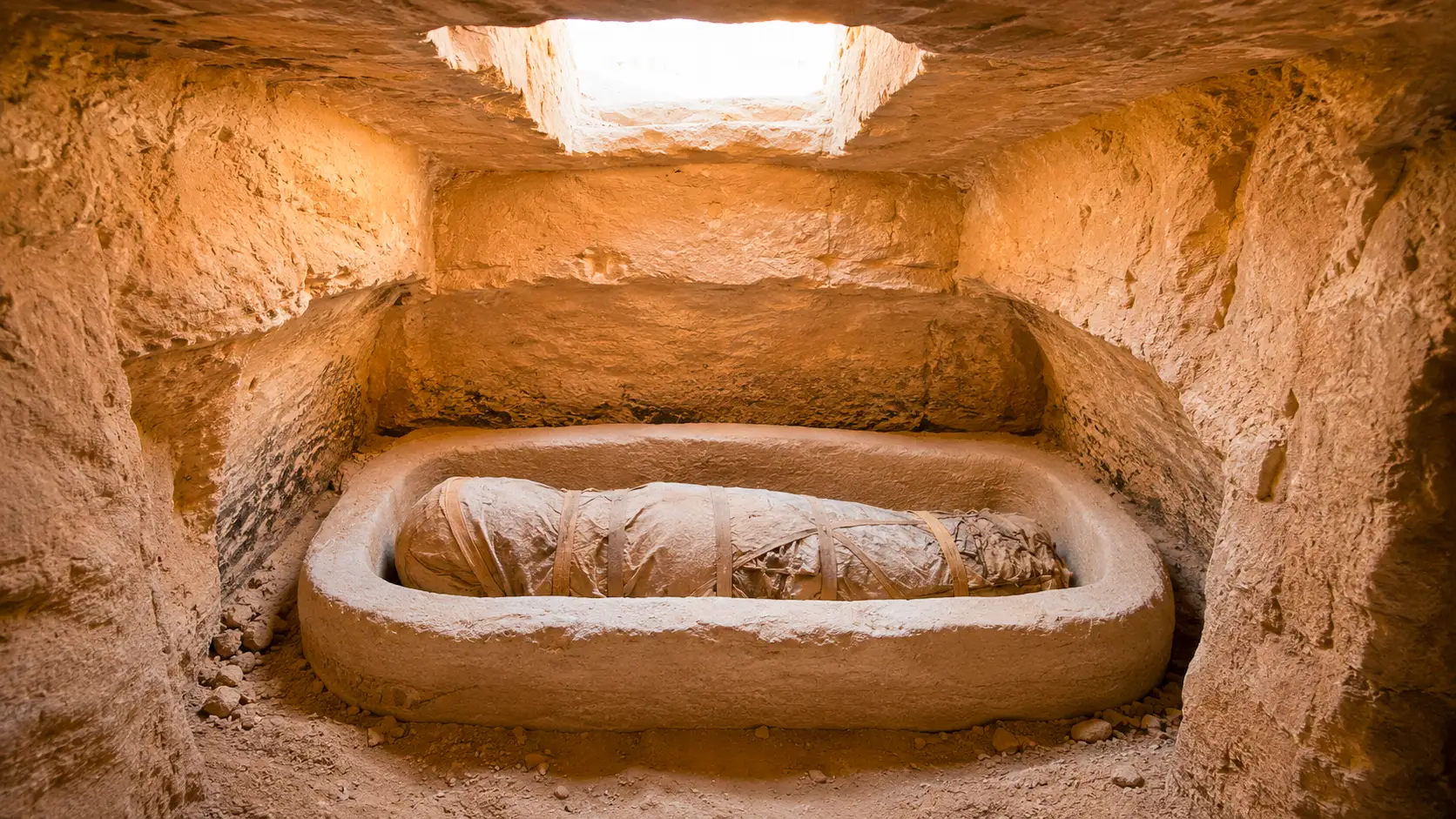 Une momie enveloppée de bandelettes repose dans un sarcophage en pierre au cœur d’une tombe creusée dans la roche à Bahariya, en Égypte.