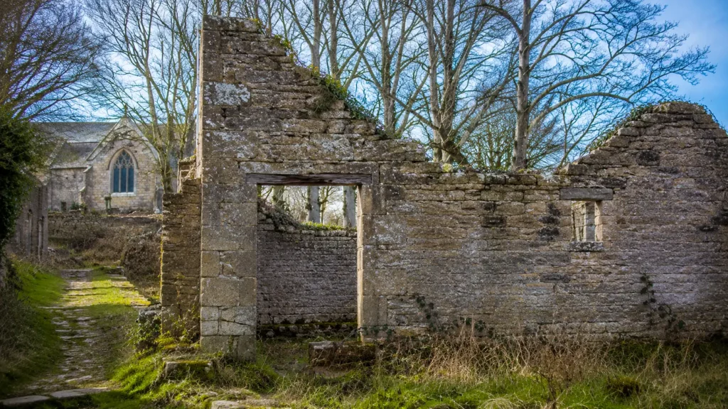 Les ruines en pierre d’une maison abandonnée de Tyneham, dans le Dorset, avec l’église St Mary visible en arrière-plan.