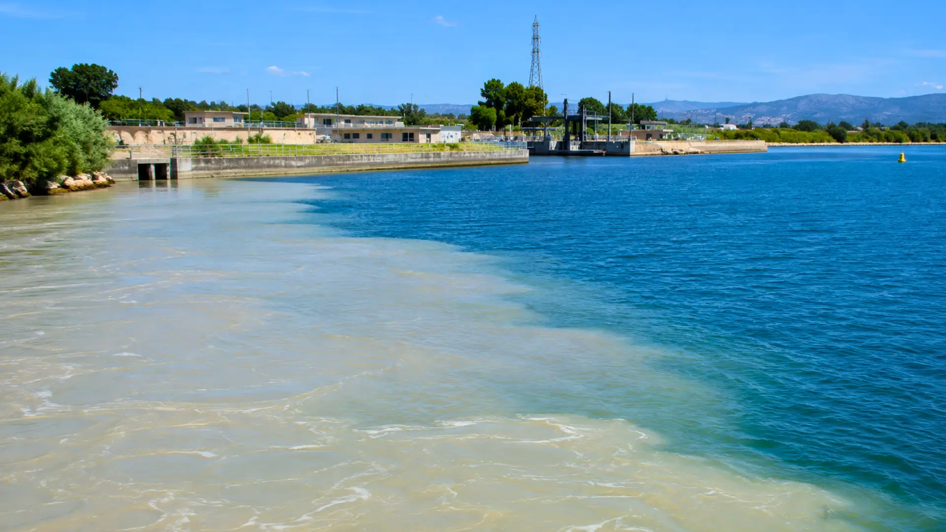 Vue de l’étang de Berre près de Saint-Chamas montrant la rencontre entre une eau douce chargée en limons et l’eau bleue de la lagune, avec le canal EDF et des infrastructures en arrière-plan.