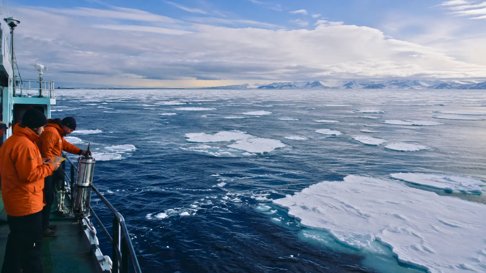 Scientifiques à bord d’un navire de recherche observant une mer couverte de glace dans une région polaire.