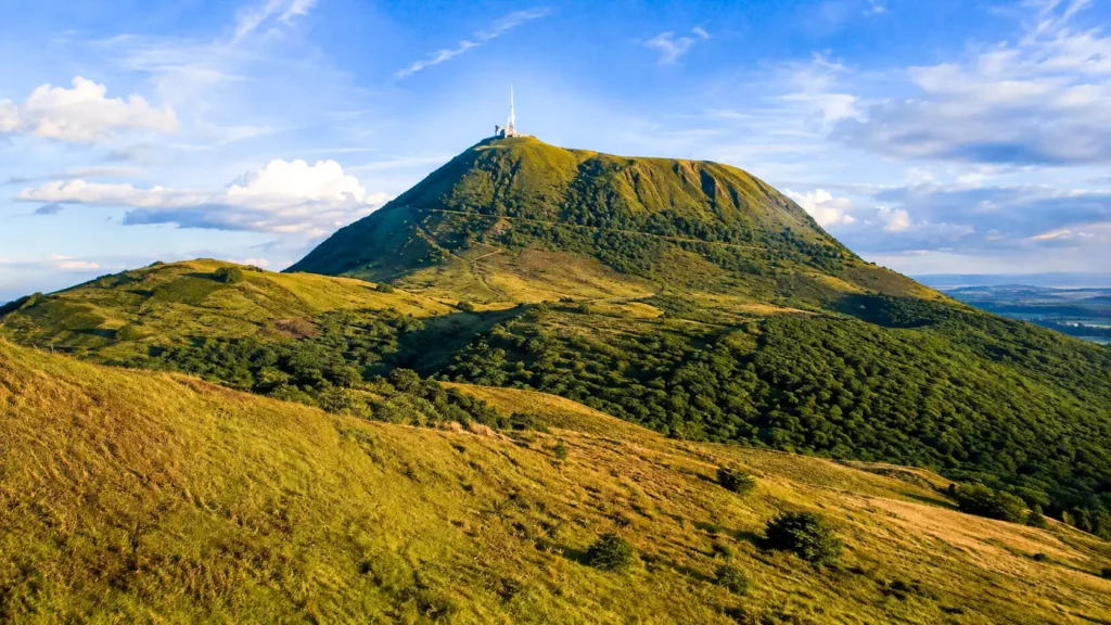 Le Puy de Dôme domine les paysages verdoyants d’Auvergne sous une lumière dorée, au cœur de la Chaîne des Puys.