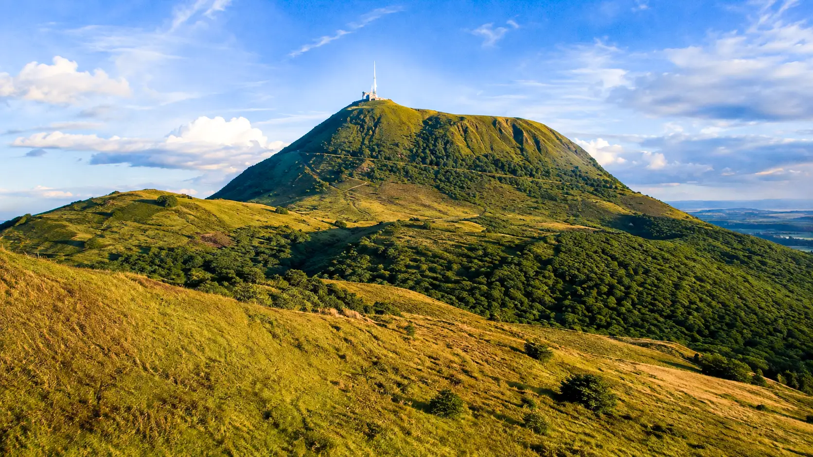 Le Puy de Dôme domine les paysages verdoyants d’Auvergne sous une lumière dorée, au cœur de la Chaîne des Puys.