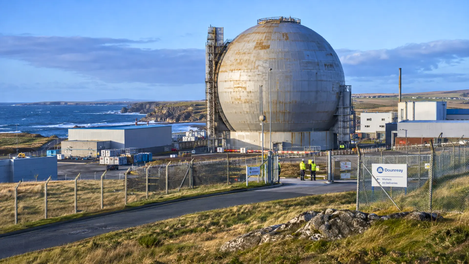 Sphère métallique de 41 mètres du réacteur nucléaire de Dounreay sur la côte écossaise, entourée d’installations industrielles et de clôtures de sécurité.