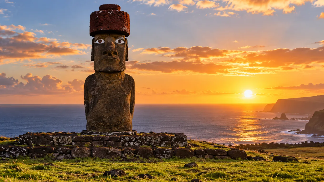 Statue Moai en pierre volcanique dressée sur sa plateforme, avec des yeux reconstitués en corail blanc et pupilles sombres, face à une prairie, l'océan derrière elle